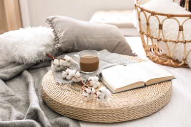 Photo of Composition with cup of drink, cotton and book on wicker pouf indoors