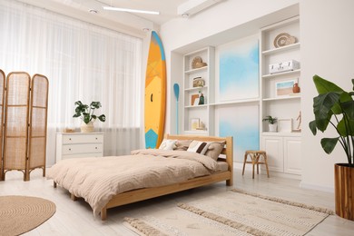 Photo of SUP board, bed and furniture in room. Interior design