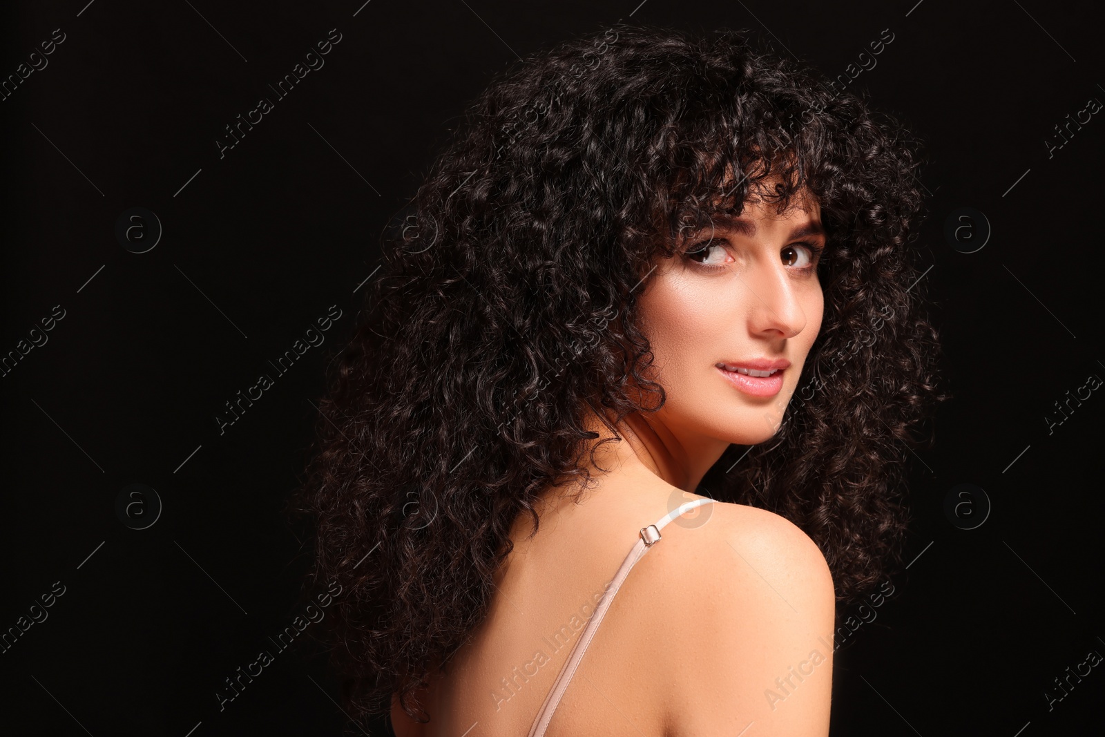 Photo of Beautiful young woman with long curly hair on black background. Space for text