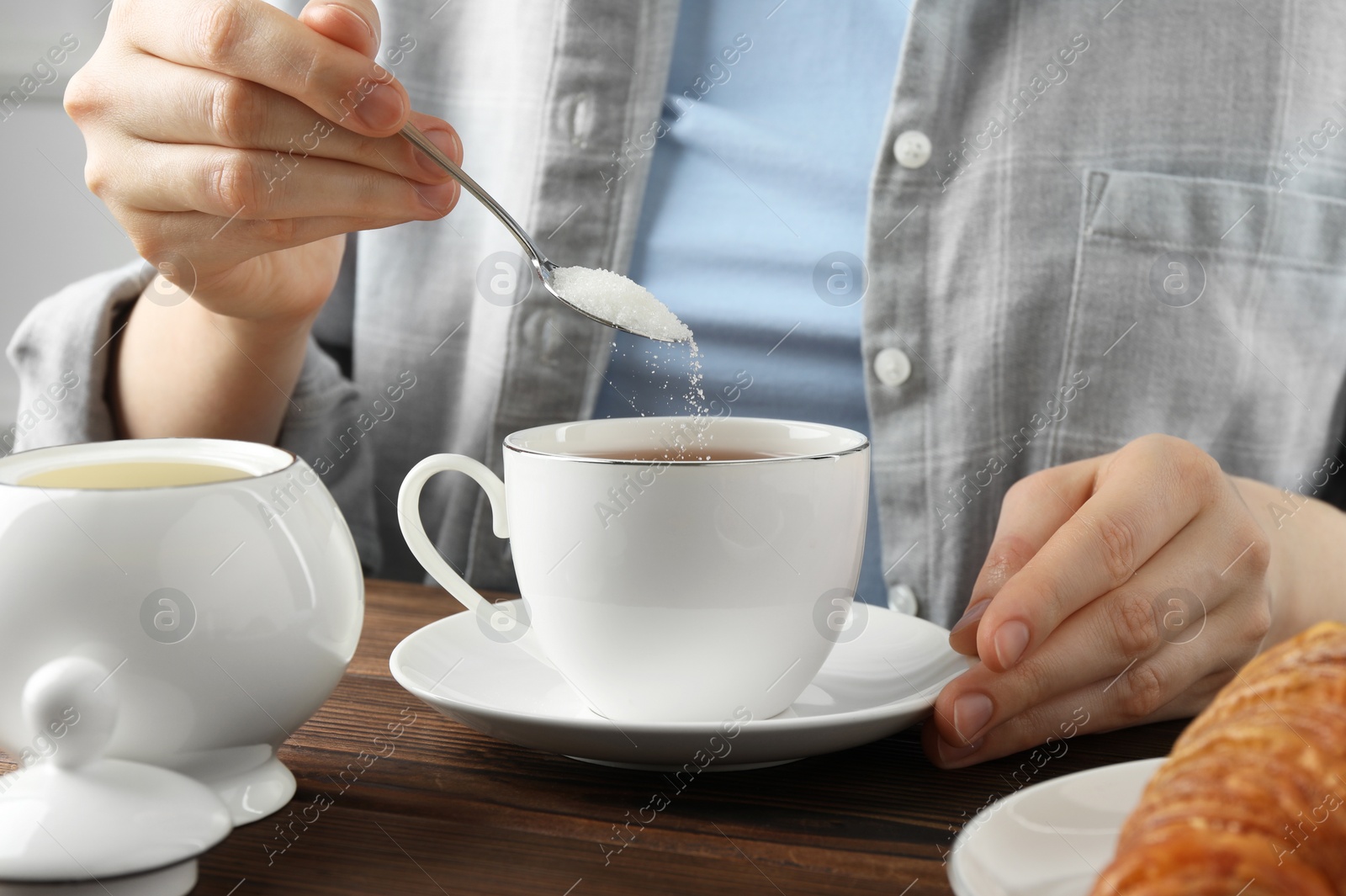 Photo of Woman adding sugar into cup of tea at wooden table, closeup