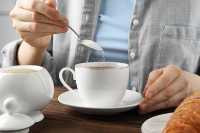 Woman adding sugar into cup of tea at wooden table, closeup
