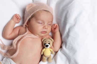 Cute little baby with toy bear sleeping on soft bed, top view