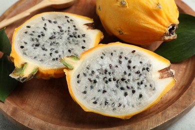 Photo of Delicious cut and whole dragon fruits (pitahaya) on wooden plate, closeup