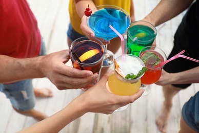 Friends clinking glasses with fresh summer cocktails outdoors, closeup