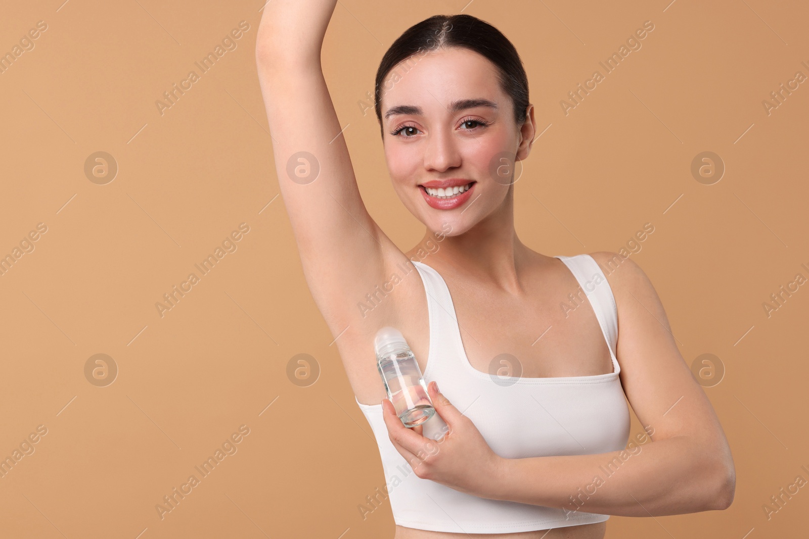 Photo of Beautiful woman applying deodorant on beige background, space for text