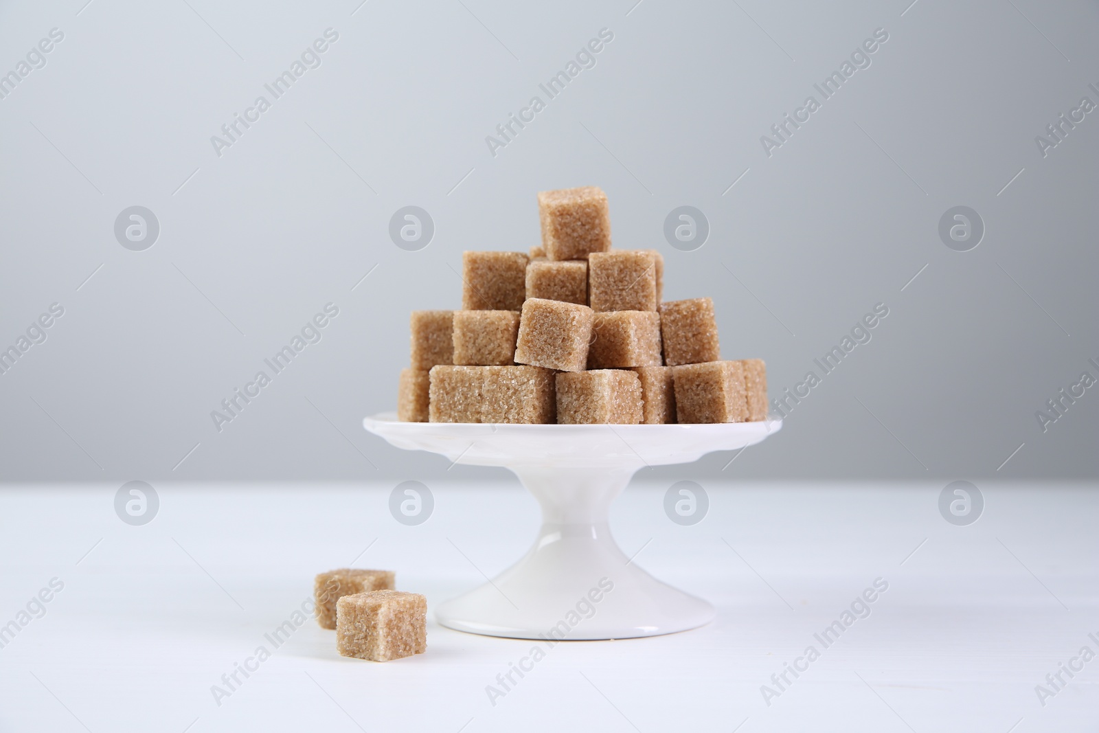 Photo of Brown sugar cubes on white table against light background