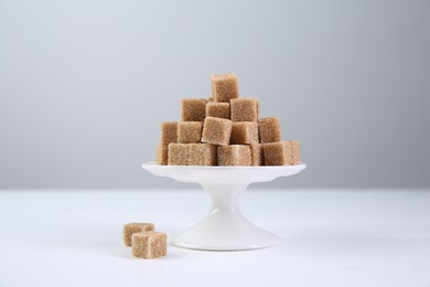 Photo of Brown sugar cubes on white table against light background