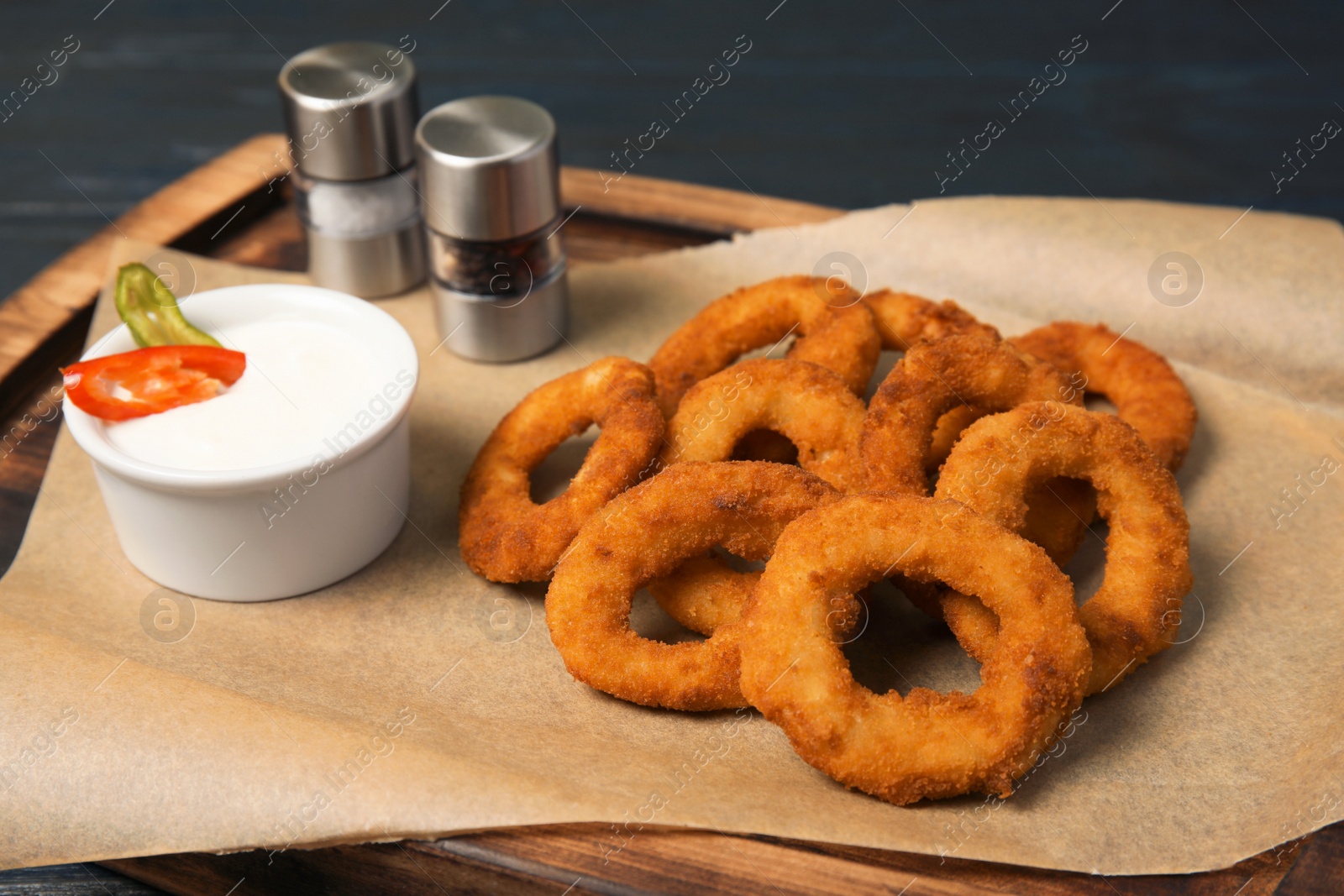 Photo of Wooden board with tasty onion rings and sauce, closeup