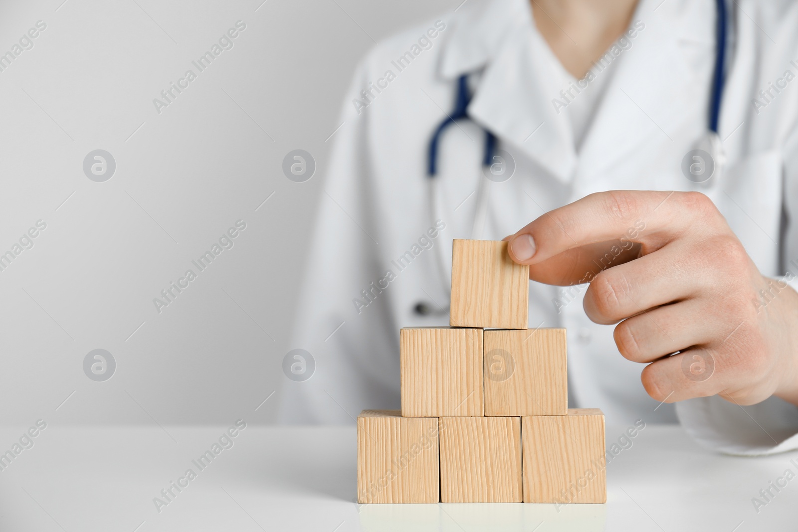 Photo of Doctor building pyramid of blank wooden cubes on white table against light background, closeup. Space for text