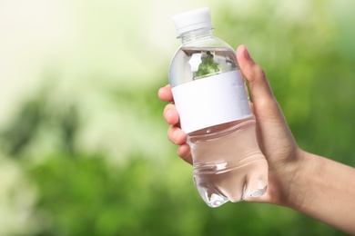 Photo of Woman holding bottle of water on blurred background. Space for text
