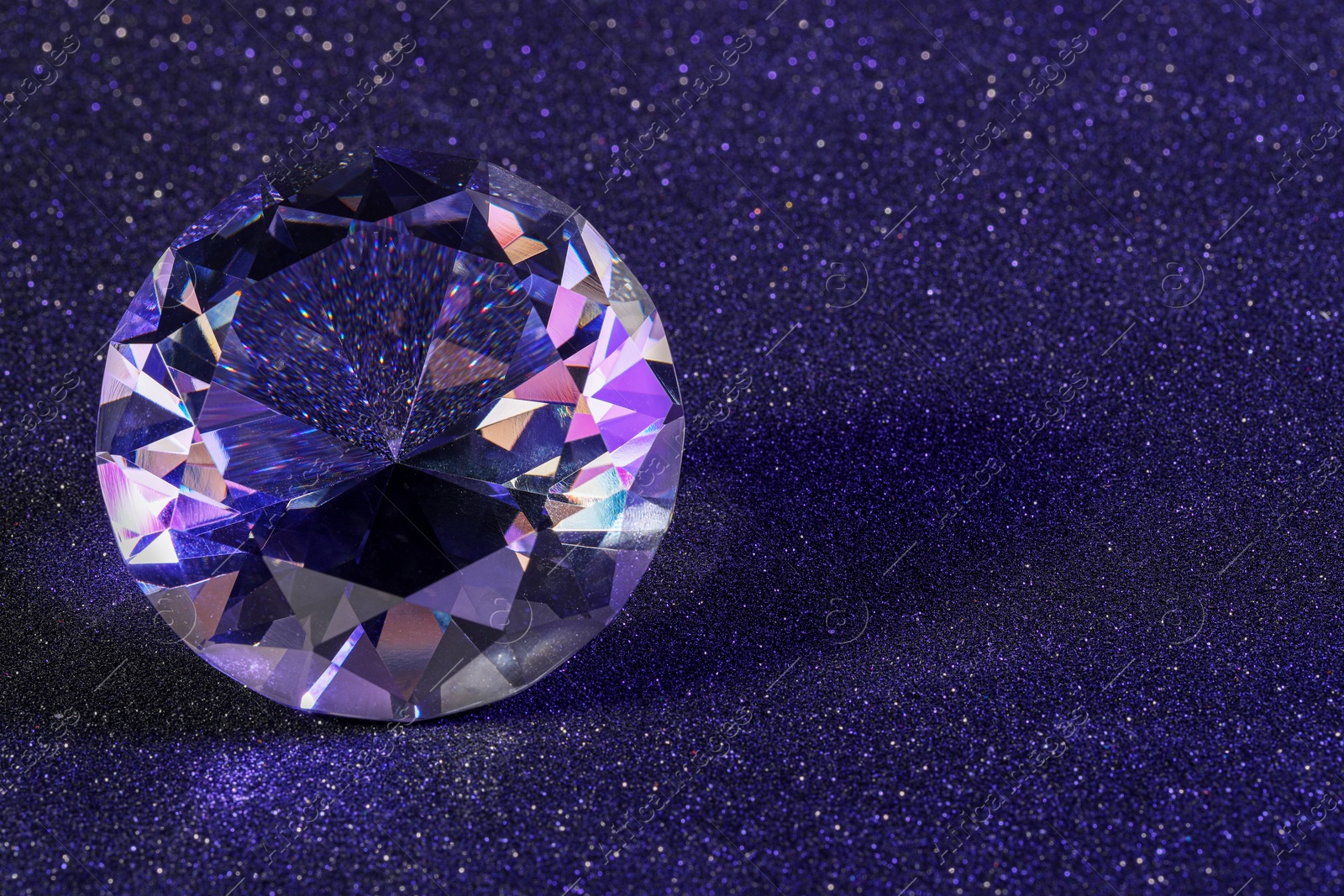 Photo of Beautiful dazzling diamond on violet glitter background, closeup. Space for text