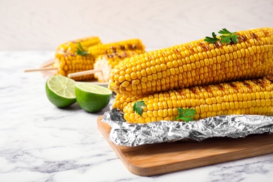 Photo of Tasty grilled corn on white marble table