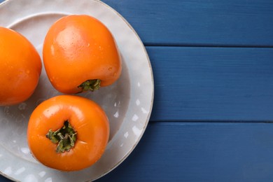 Photo of Delicious ripe persimmons on blue wooden table, top view. Space for text