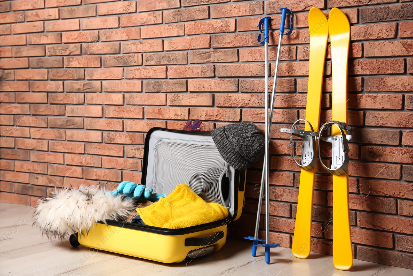 Photo of Suitcase with clothes, camera and skis on floor against brick wall, space for text. Winter vacation