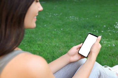 Photo of Woman using smartphone on green grass outdoors, closeup