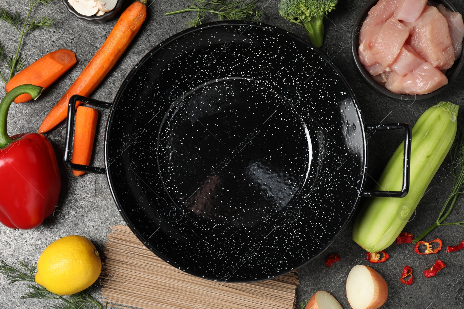 Photo of Empty iron wok surrounded by ingredients on grey table, flat lay