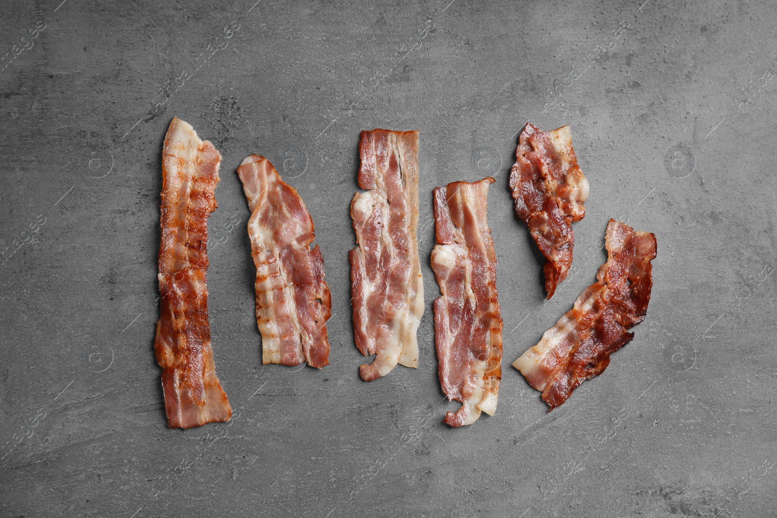 Photo of Slices of tasty fried bacon on dark background, flat lay