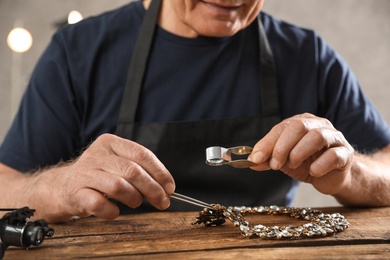 Male jeweler evaluating necklace at table in workshop, closeup