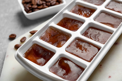 Photo of Ice cubes in tray and coffee beans on grey table, closeup