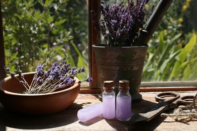 Photo of Beautiful lavender flowers, scissors and bottles with essence oil on wooden table indoors