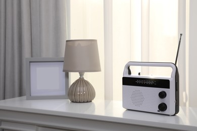 Stylish radio receiver, lamp and frame on white table near window indoors