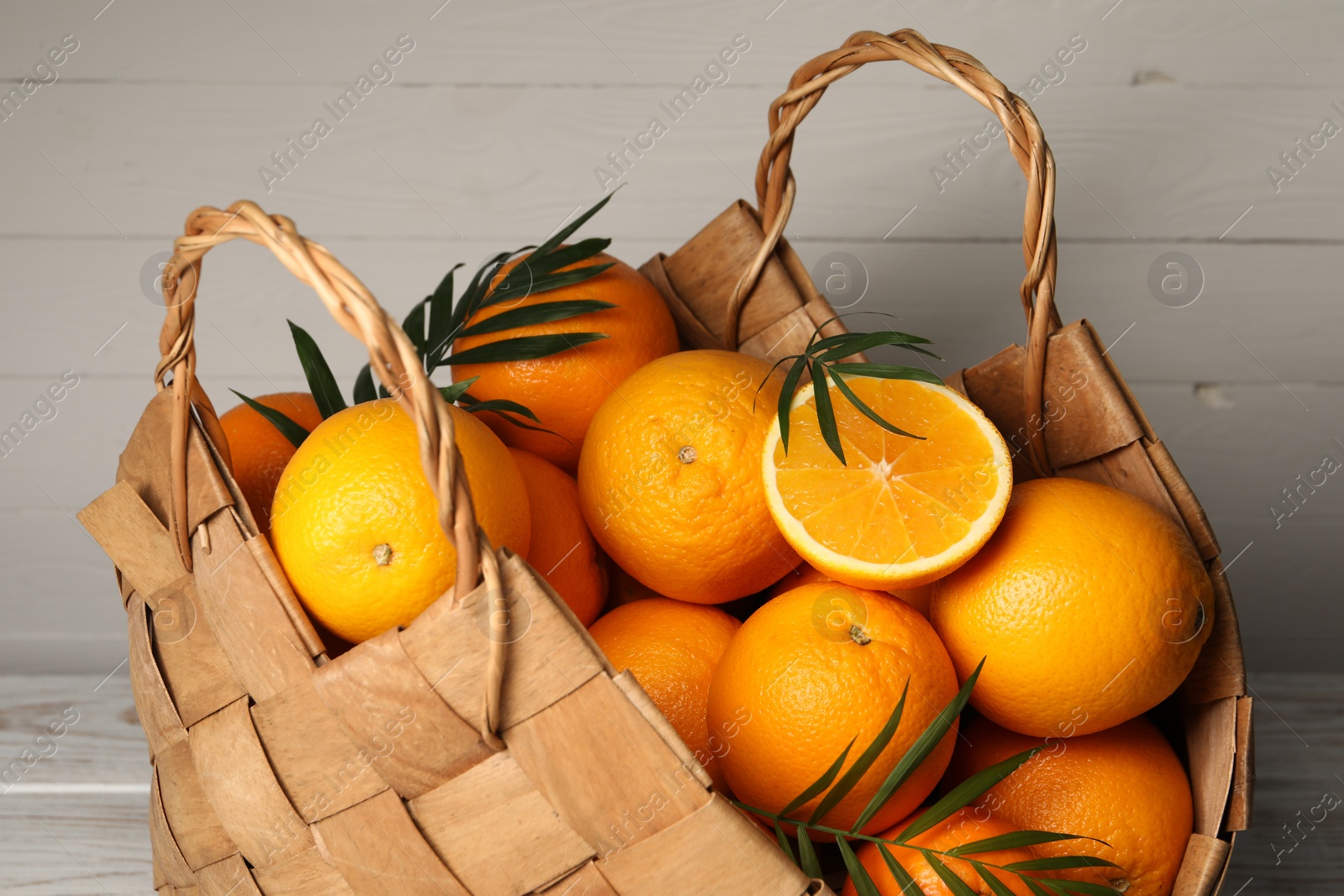 Photo of Wicker basket with whole and cut ripe oranges on wooden background, closeup