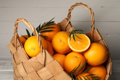 Wicker basket with whole and cut ripe oranges on wooden background, closeup