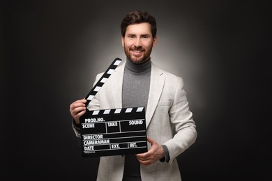 Photo of Smiling actor holding clapperboard on black background