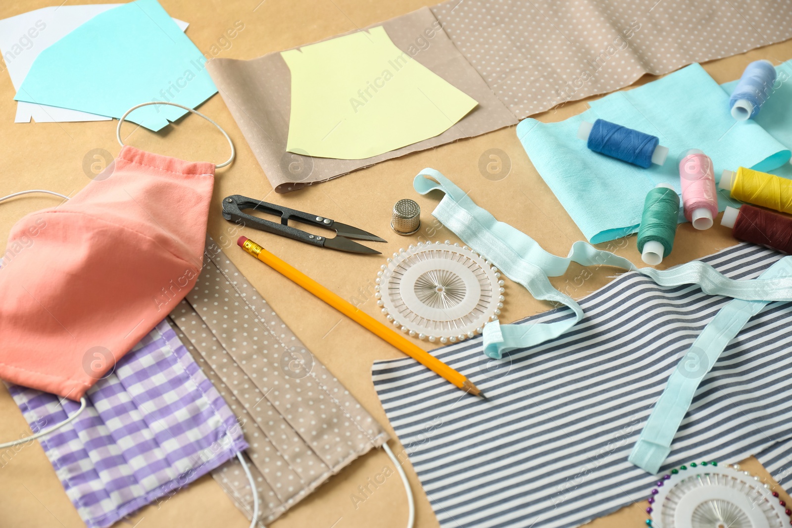 Photo of Fabric, sewing accessories and cloth masks on brown background. Personal protective equipment during COVID-19 pandemic