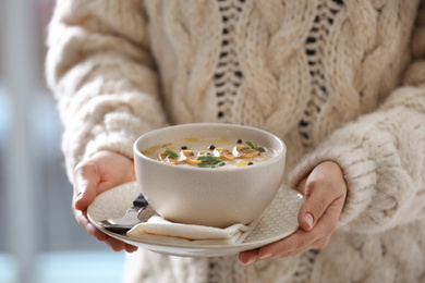 Young woman with bowl of cream soup on blurred background, closeup