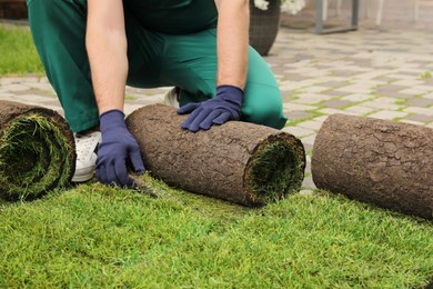 Photo of Worker unrolling grass sods on pavement at backyard, closeup