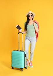 Photo of Beautiful woman with suitcase and ticket in passport for summer trip on yellow background. Vacation travel