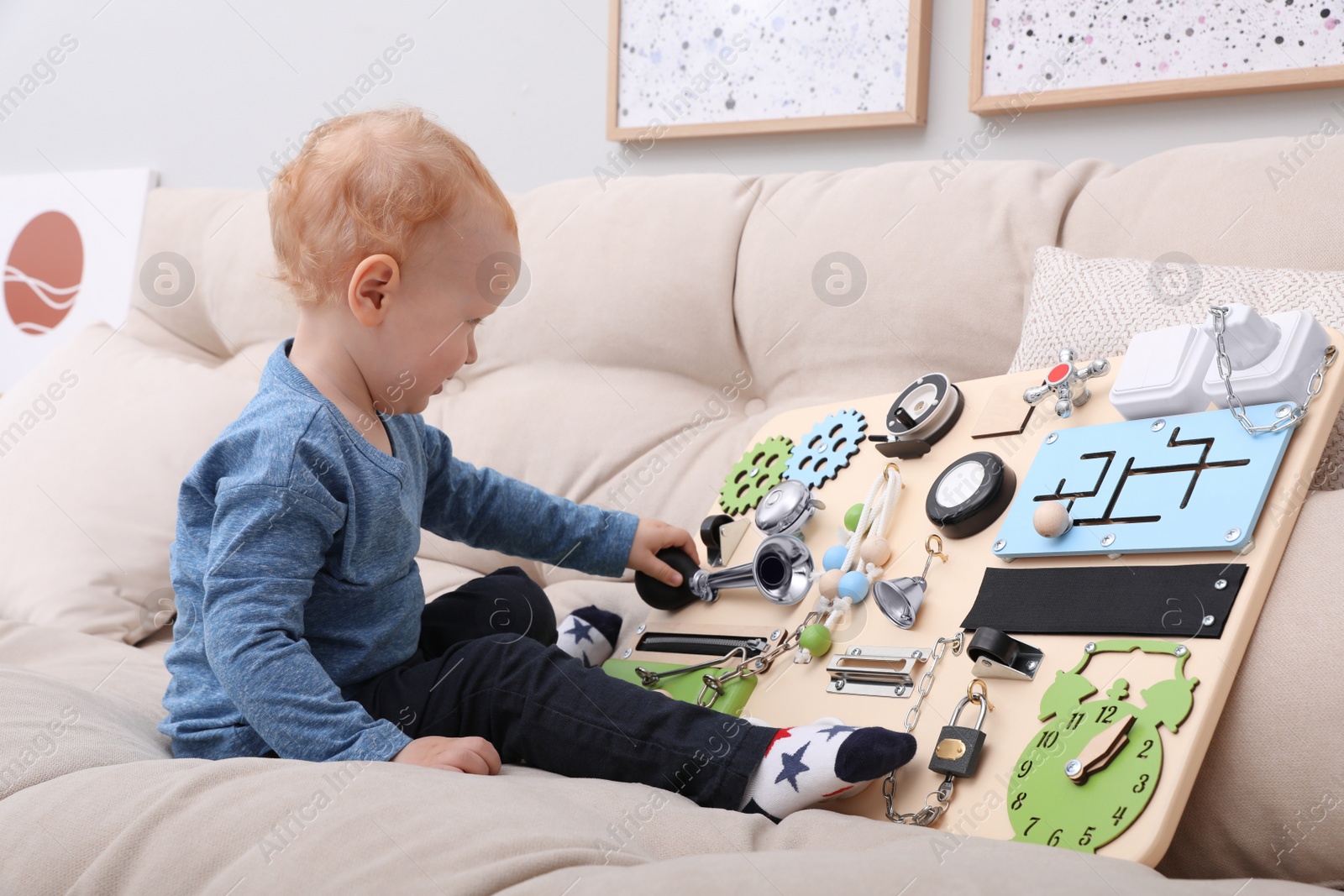 Photo of Cute little boy playing with busy board on sofa at home