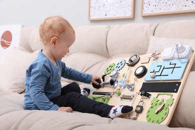 Photo of Cute little boy playing with busy board on sofa at home