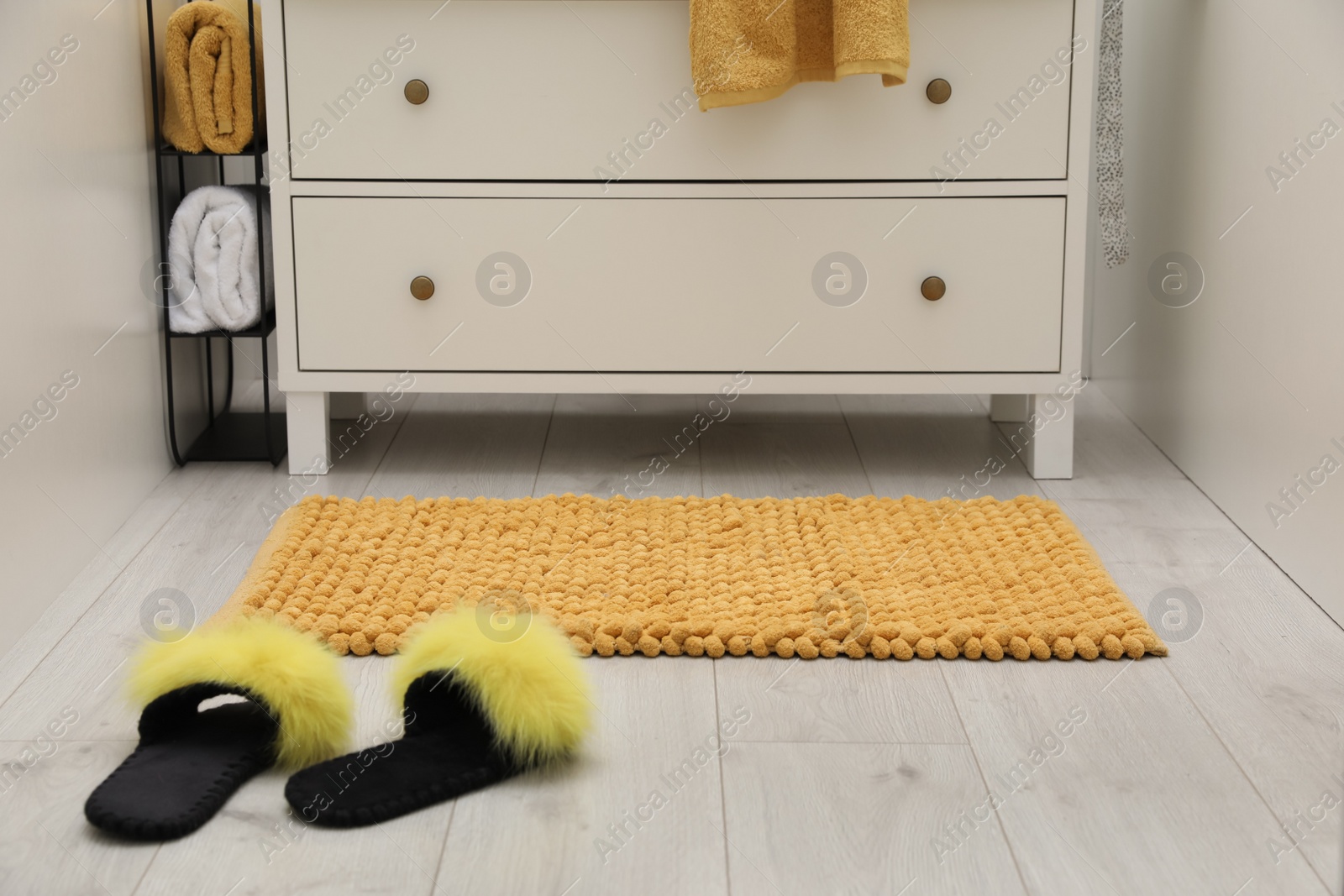 Photo of Orange bath mat and slippers near chest of drawers indoors