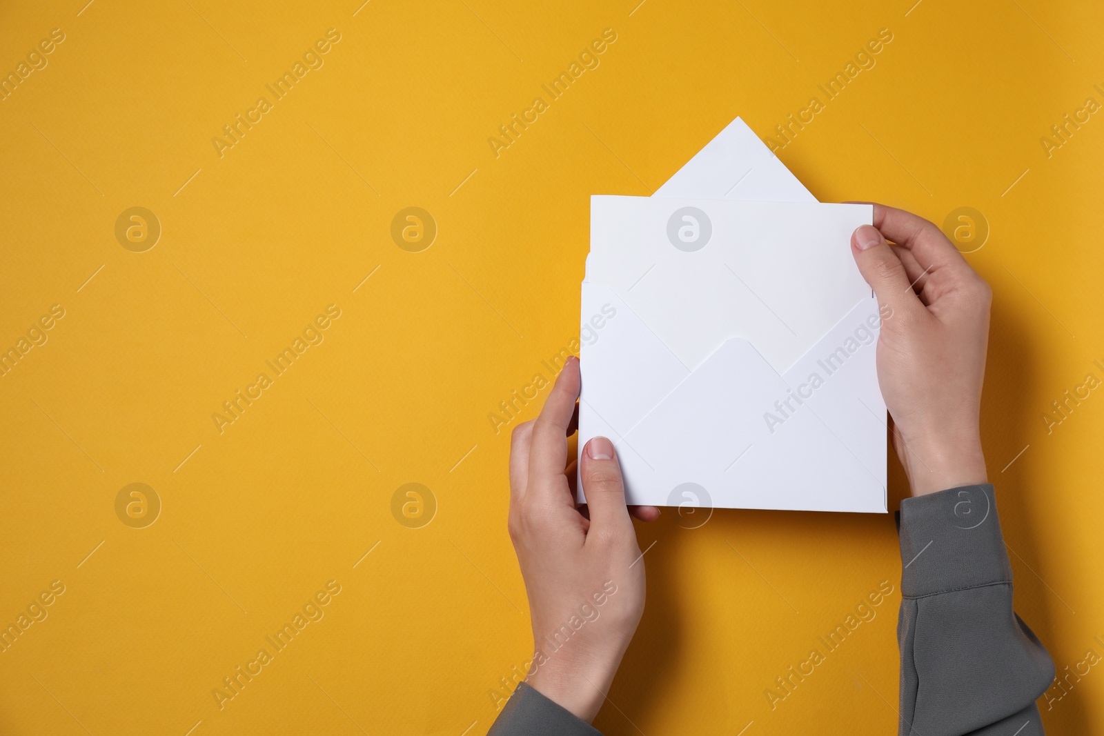 Photo of Woman taking card out of letter envelope at orange table, top view. Space for text