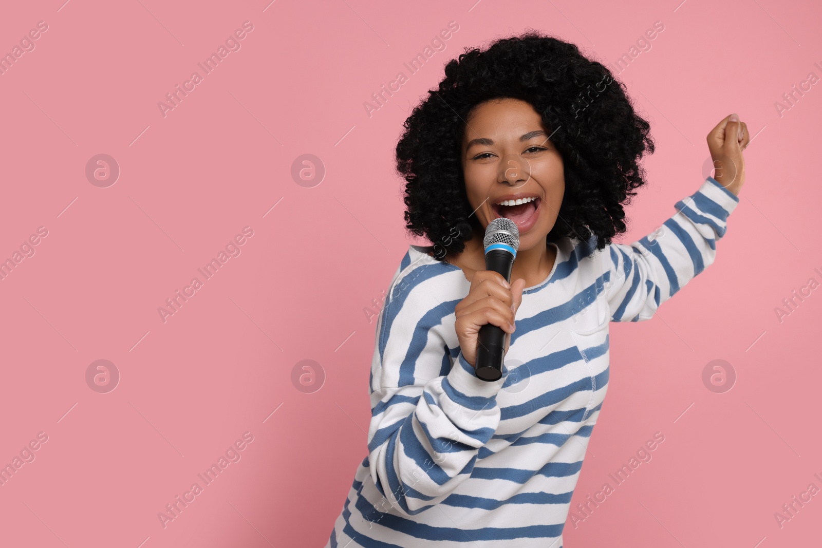 Photo of Beautiful woman with microphone singing on pink background, space for text