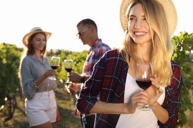 Photo of Beautiful young woman with glass of wine and her friends in vineyard on sunny day