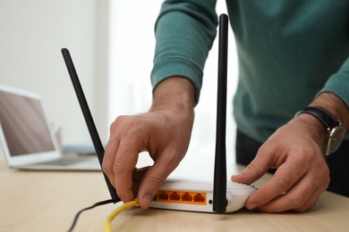 Photo of Man connecting cable to router at wooden table indoors, closeup. Wireless internet communication