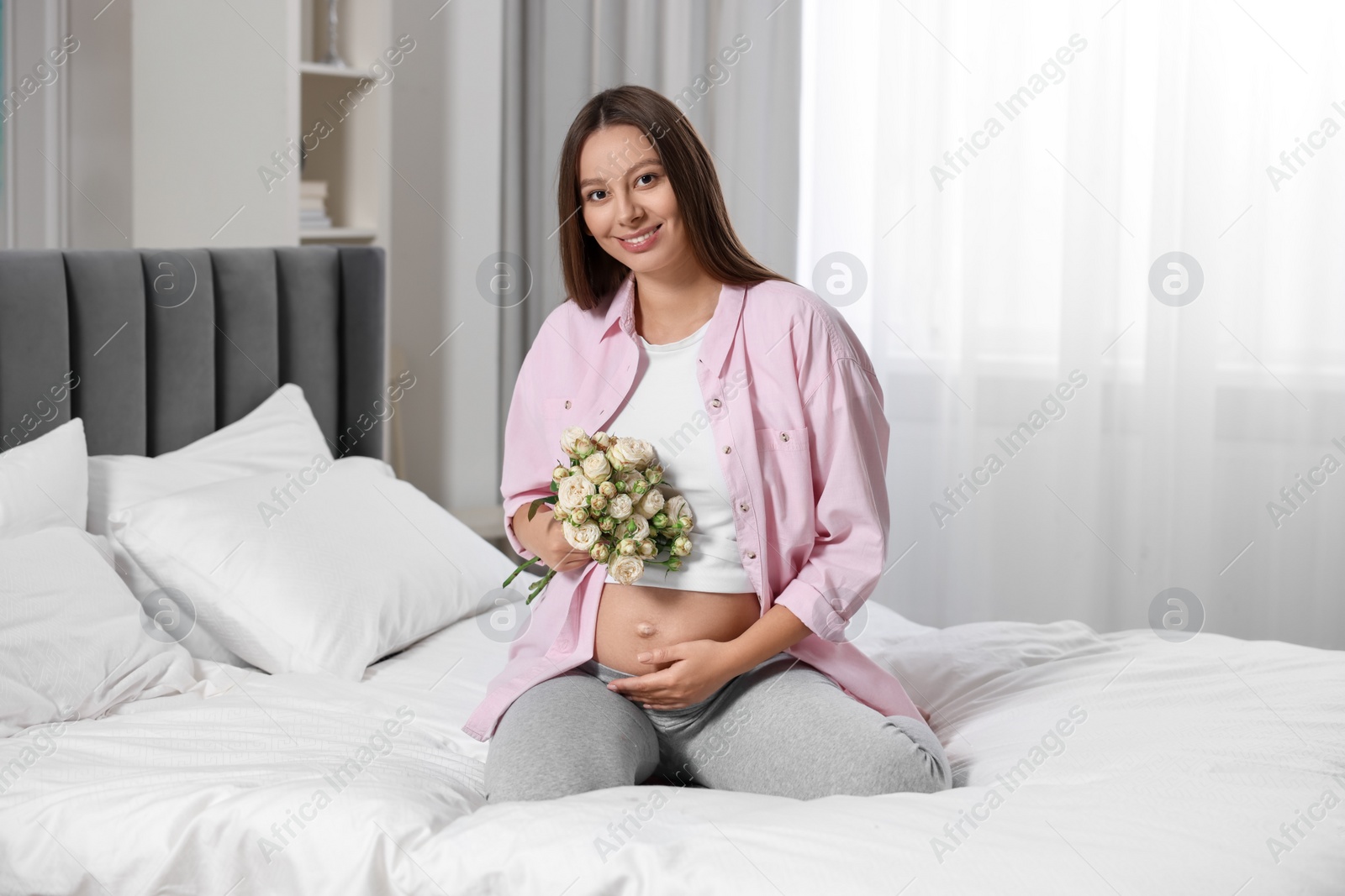 Photo of Beautiful pregnant woman with bouquet of roses in bedroom