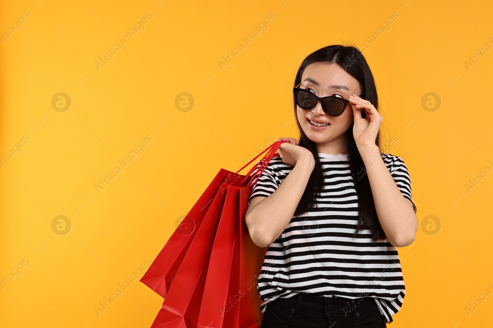 Photo of Smiling woman with shopping bags on yellow background. Space for text