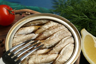 Tin can with tasty sprats and products on wooden board, closeup