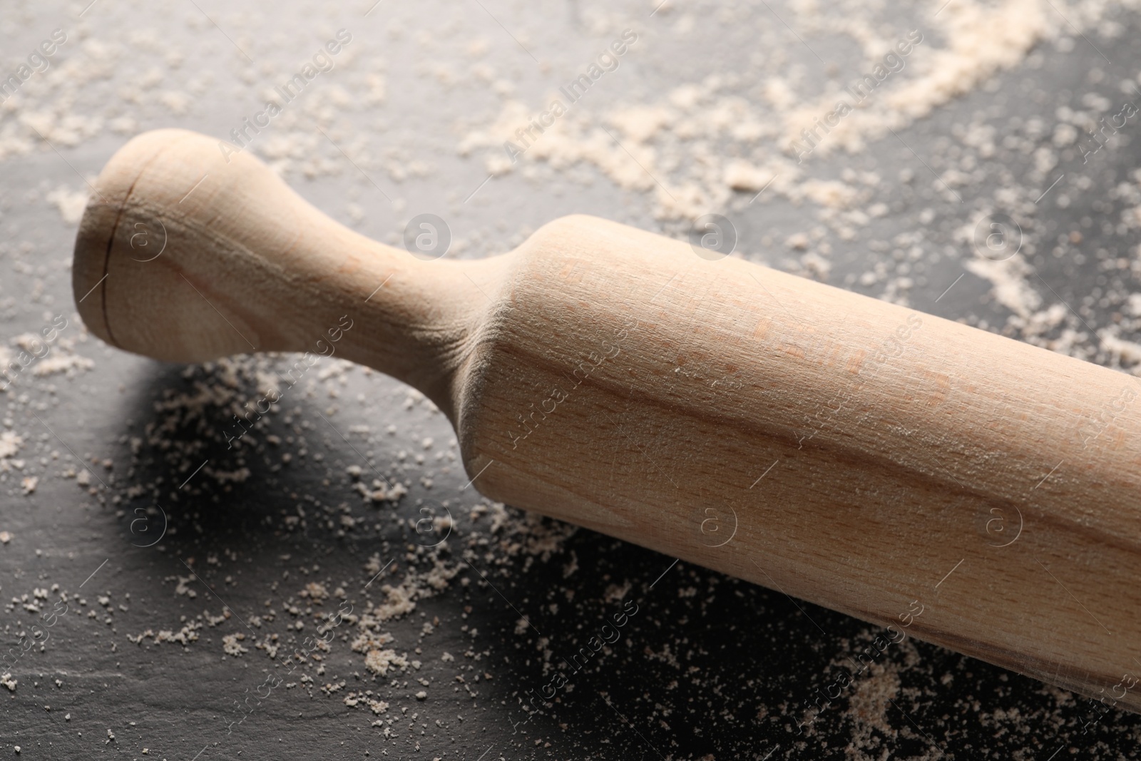 Photo of Scattered flour and rolling pin on dark textured table, closeup