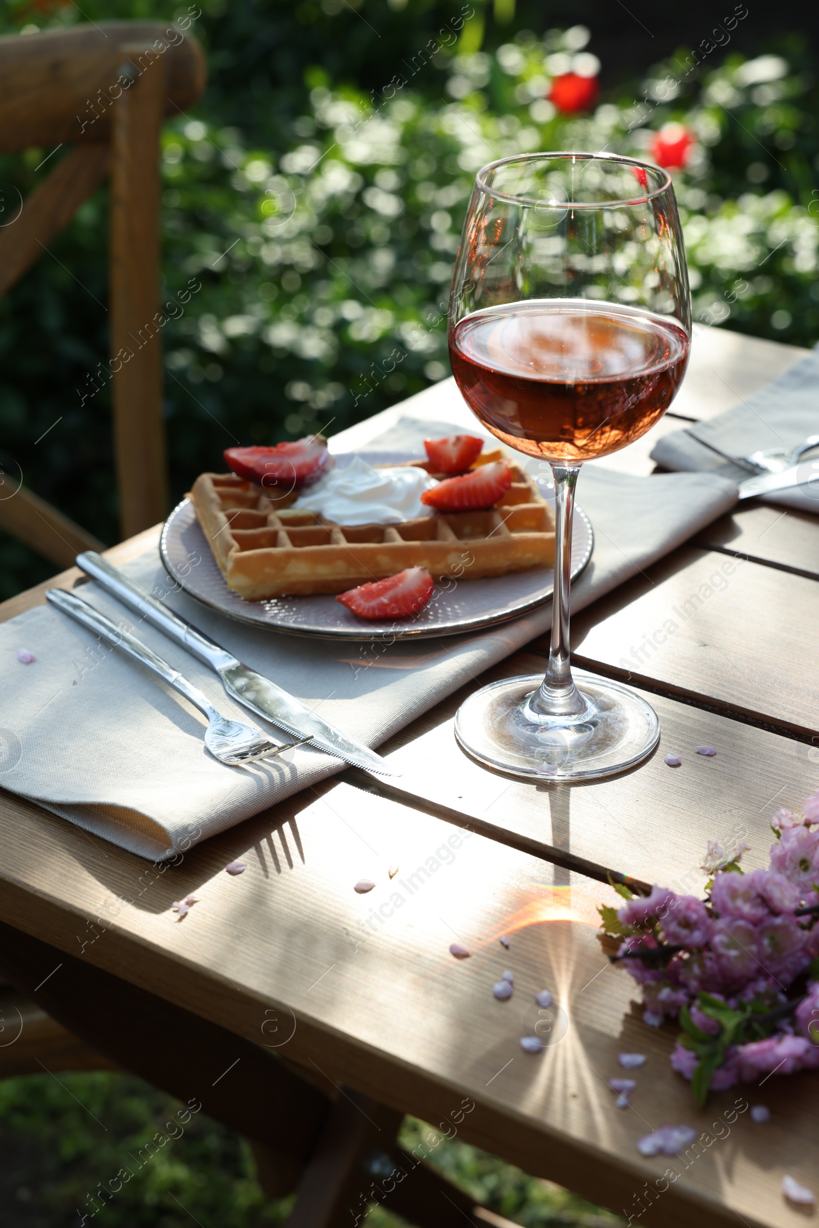 Photo of Delicious Belgian waffles with fresh strawberries and wine served on table in garden