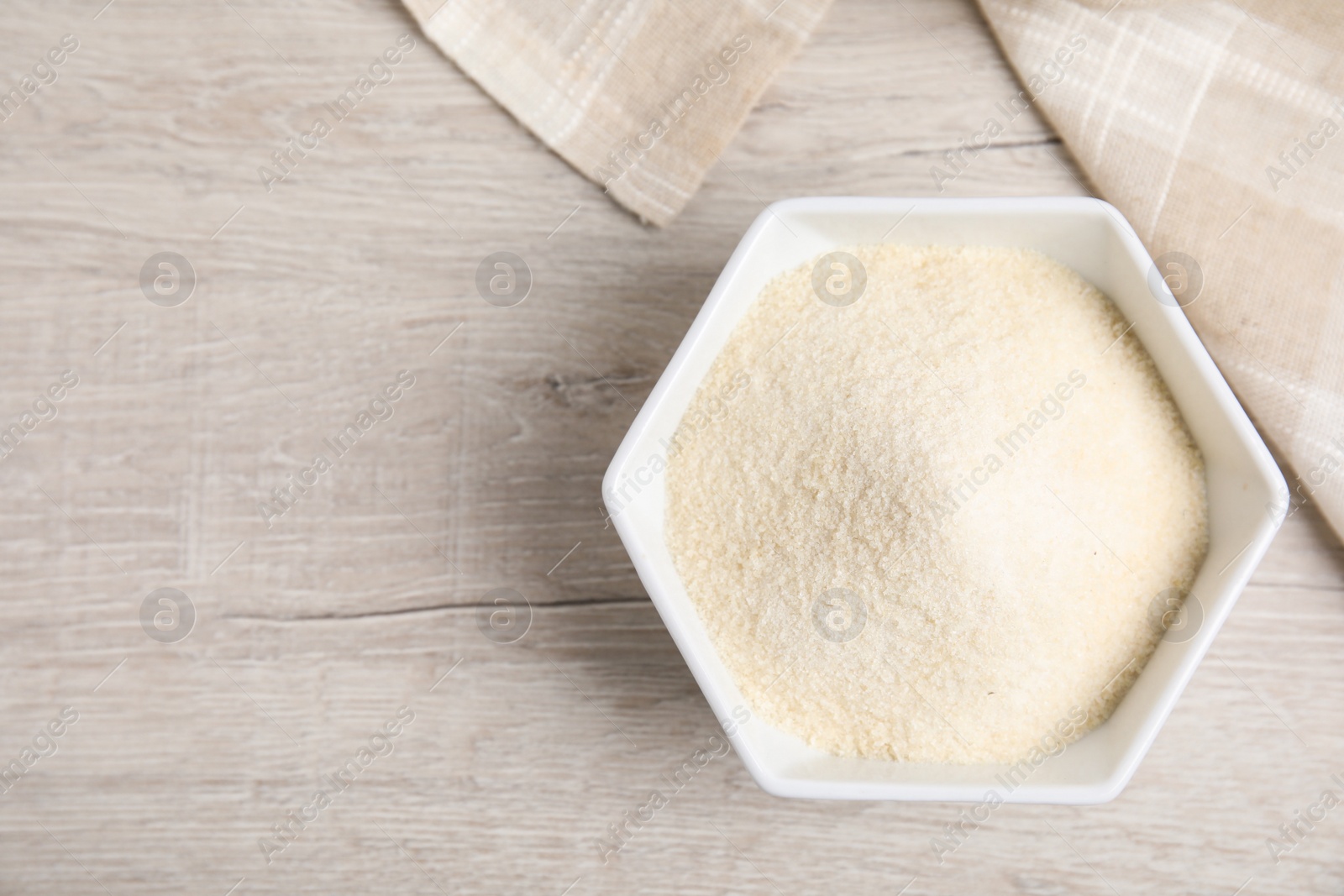 Photo of Gelatin powder in bowl on white wooden table, top view. Space for text