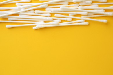 Many clean cotton buds on yellow background, flat lay. Space for text