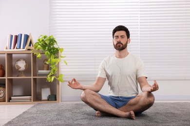 Photo of Man in earphones meditating at home, space for text