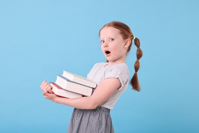 Photo of Surprised girl with stack of books on light blue background