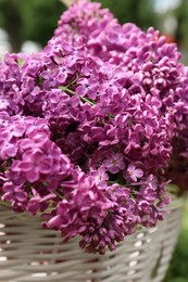 Photo of Beautiful lilac flowers in wicker basket outdoors, closeup
