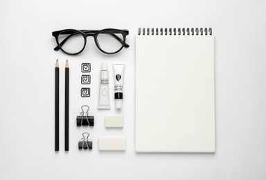 Photo of Composition with sketchbook, glasses and stationary on white background, top view